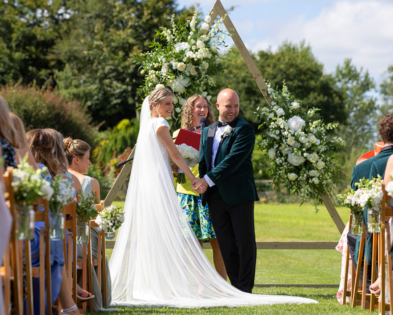Devon Wedding Celebrant conducting a service outside with a lush green background.